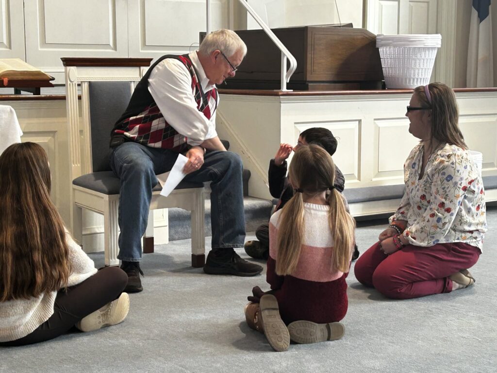 A church leader sharing the children's message with kids gathered around