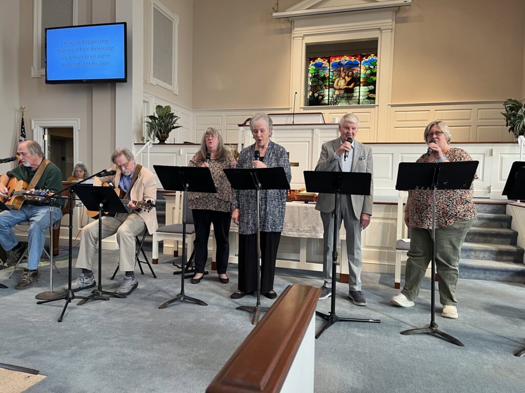 A small praise team of vocalists and guitars leading a Sunday hymn